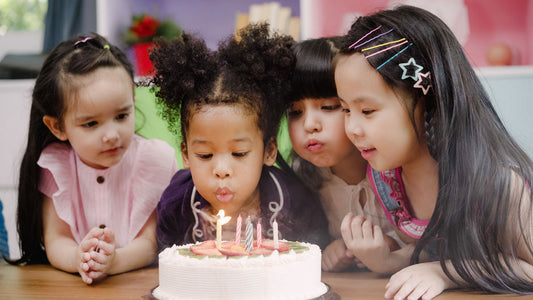Happy children gathered around a birthday cake, watching as the birthday girl blows out her candles.